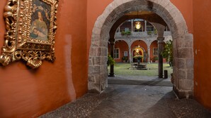 Una entrada arquejada que condueix a un pati amb una font, envoltat de parets de pedra i plantes en testos.
