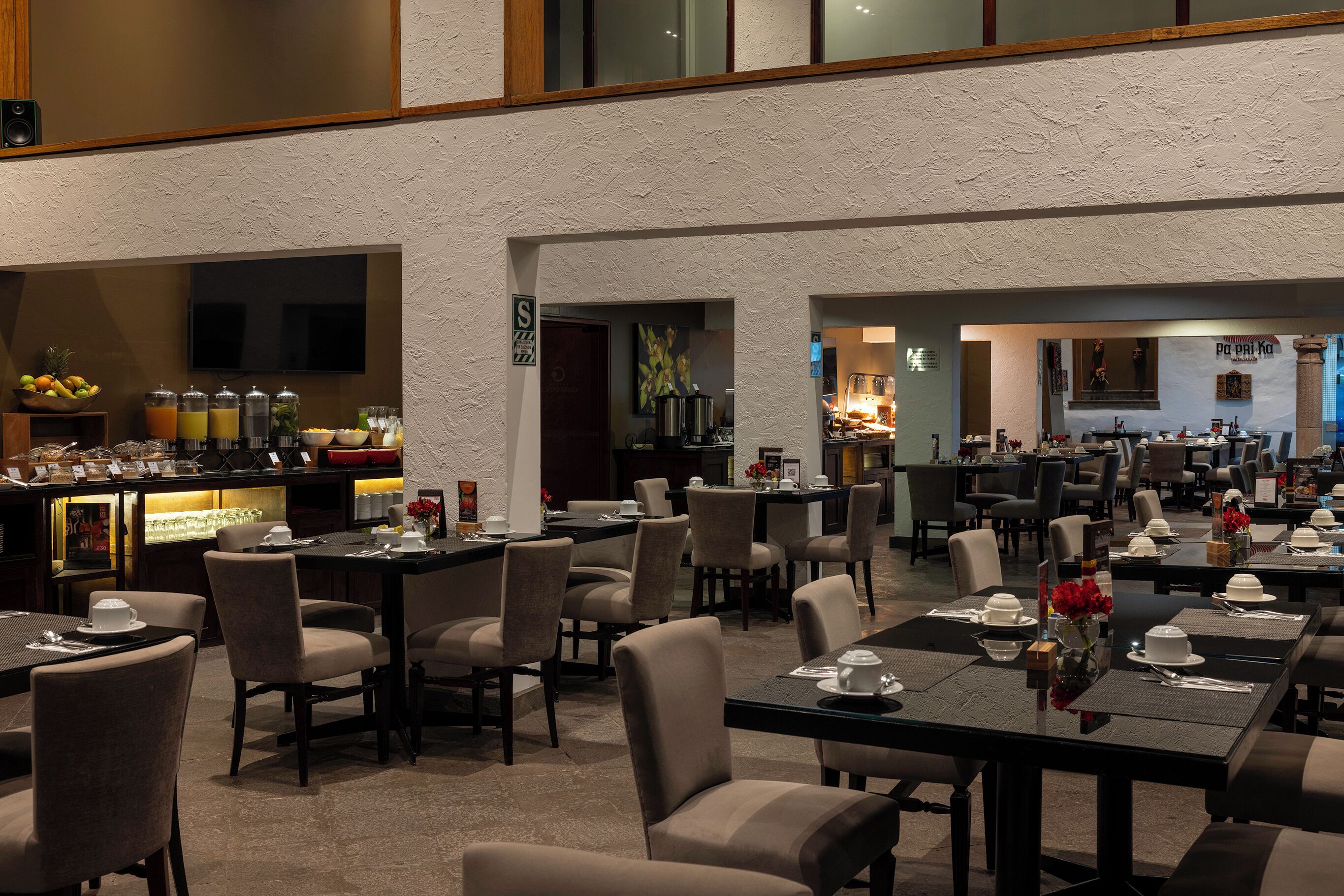 Uma ampla área de refeições com várias mesas e cadeiras, um bar com diversas bebidas e uma cozinha visível ao fundo.