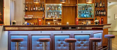 Una zona de bar con mostrador de madera, estantes con botellas y taburetes.