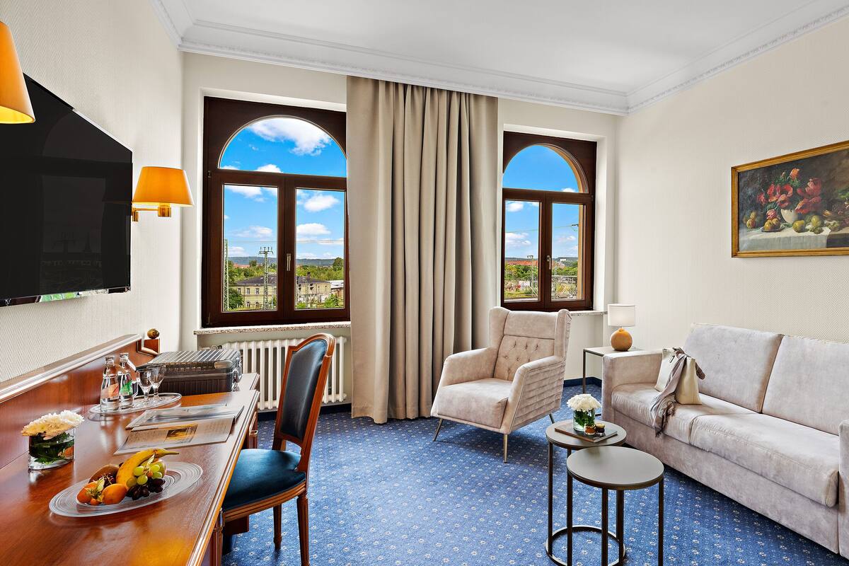 Une chambre d’hôtel comprenant un coin repas, un canapé, un fauteuil, une petite table et un tableau au mur.