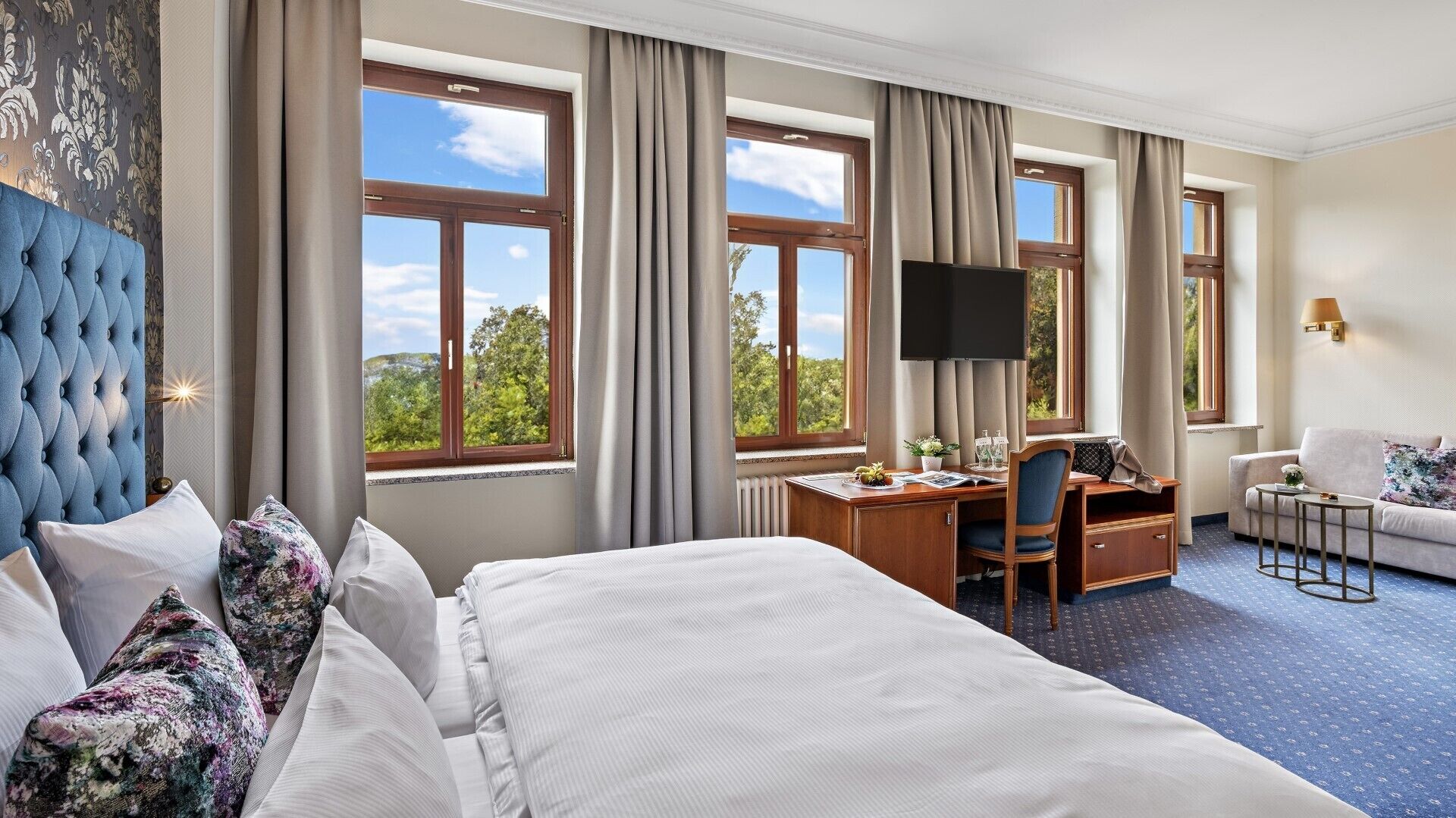 Camera d'albergo con un letto grande, una scrivania con una sedia, una TV e un divano.