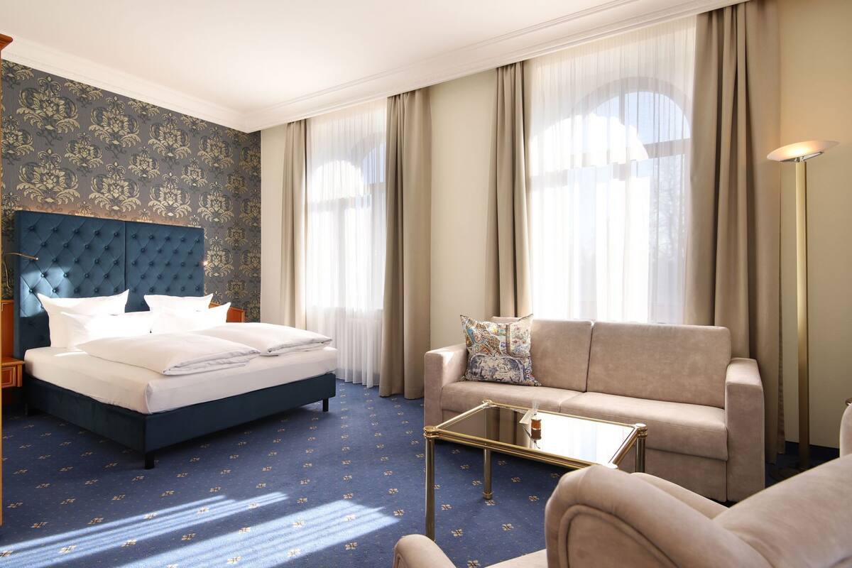 Une chambre d’hôtel avec un lit, un canapé, une table basse et de grandes fenêtres avec des rideaux.