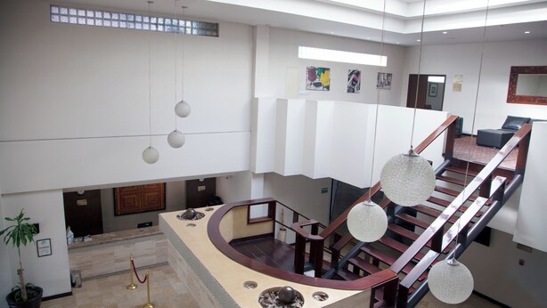 A spacious lobby with a central staircase, a reception desk, and a potted plant.