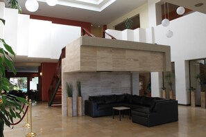 A spacious lobby with a black leather sofa, a small table, and a staircase leading to an upper level.