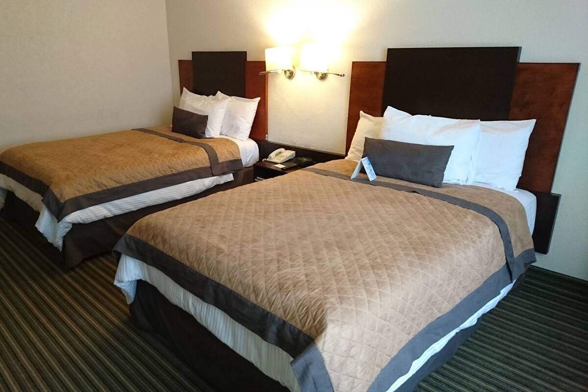 A hotel room with two beds, a nightstand, a telephone, and a wall-mounted light fixture.
