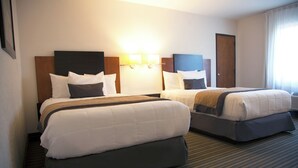 A hotel room with two beds, a headboard with a light fixture, and a carpeted floor.