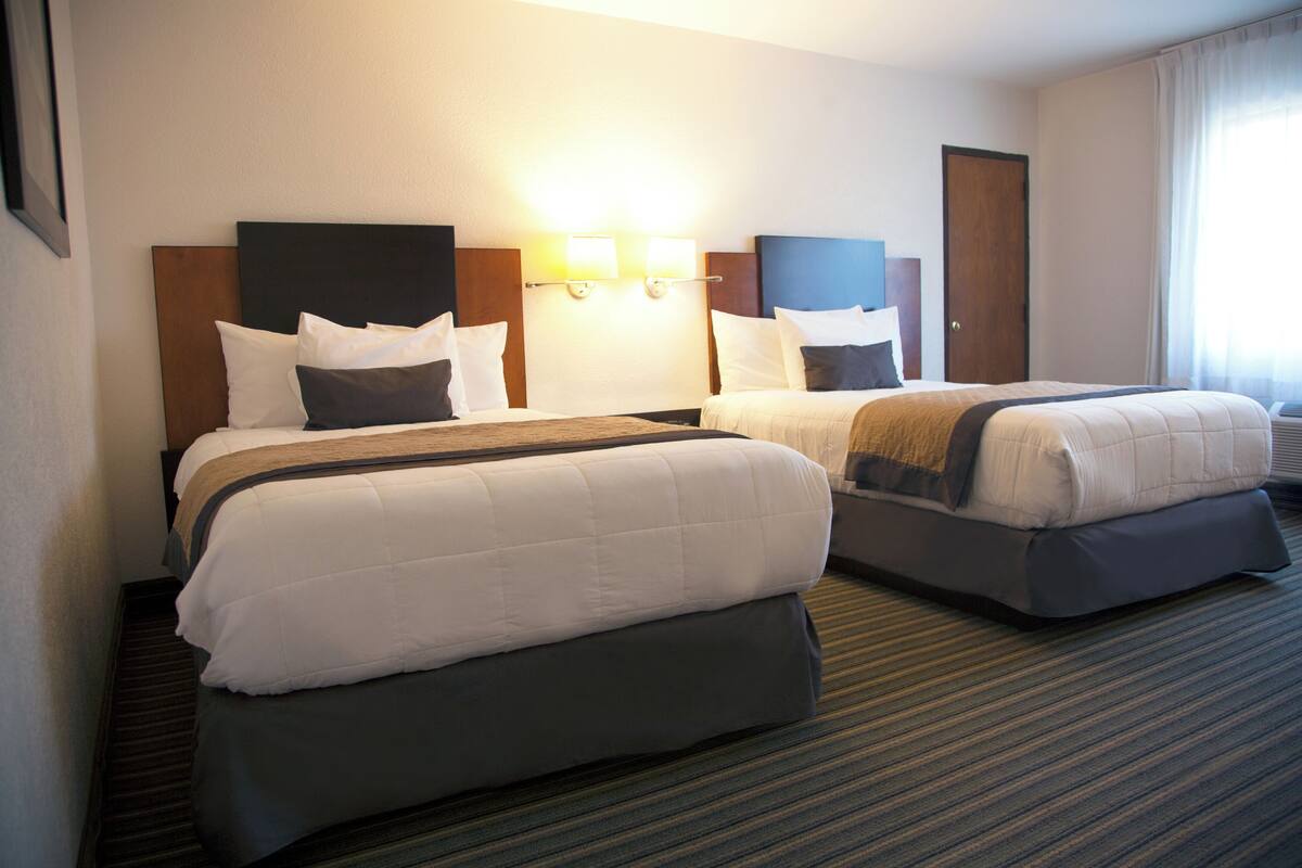 A hotel room with two beds, a headboard with a light fixture, and a carpeted floor.
