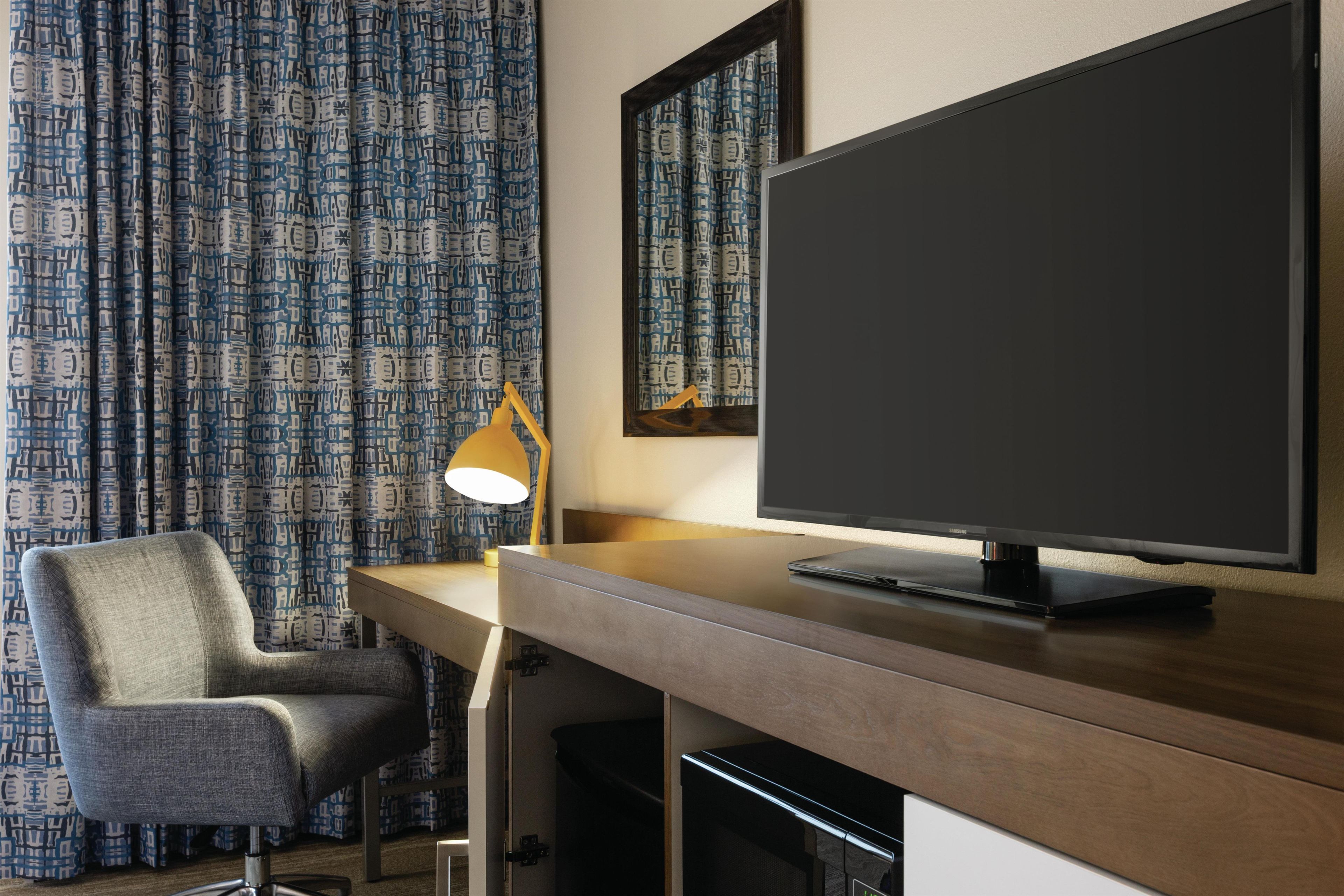 A hotel room with a desk, a chair, a television, and patterned curtains.