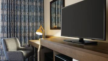 A hotel room with a desk, a chair, a television, and patterned curtains.