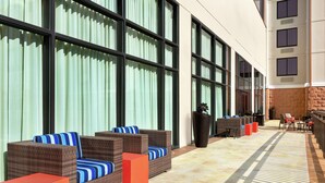 A covered outdoor seating area with wicker furniture and red accents, large windows, and a tiled floor. - Hampton Inn & Suites Dallas-Mesquite (Mesquite)