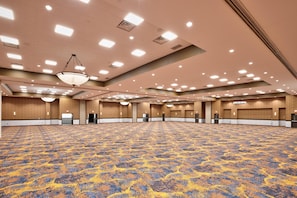 Une grande salle de conférence dotée d’un tapis à motifs, d’un éclairage encastré et de lambris en bois.