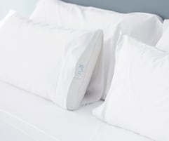 Una cama blanca con almohadas, una de ellas con la etiqueta que dice "Pure".