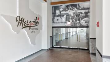 Un pasillo con una puerta de vidrio que da a una habitación, una pared con el texto 'Mesquite Convention Center' y un cartel con una persona montando a caballo.