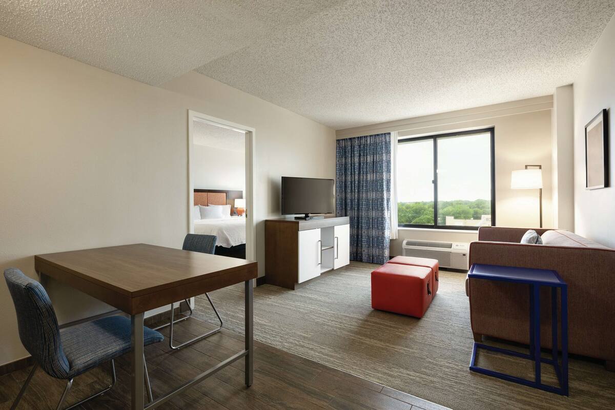 Habitación de hotel con escritorio de madera, televisor, sofá y ventana con vistas.