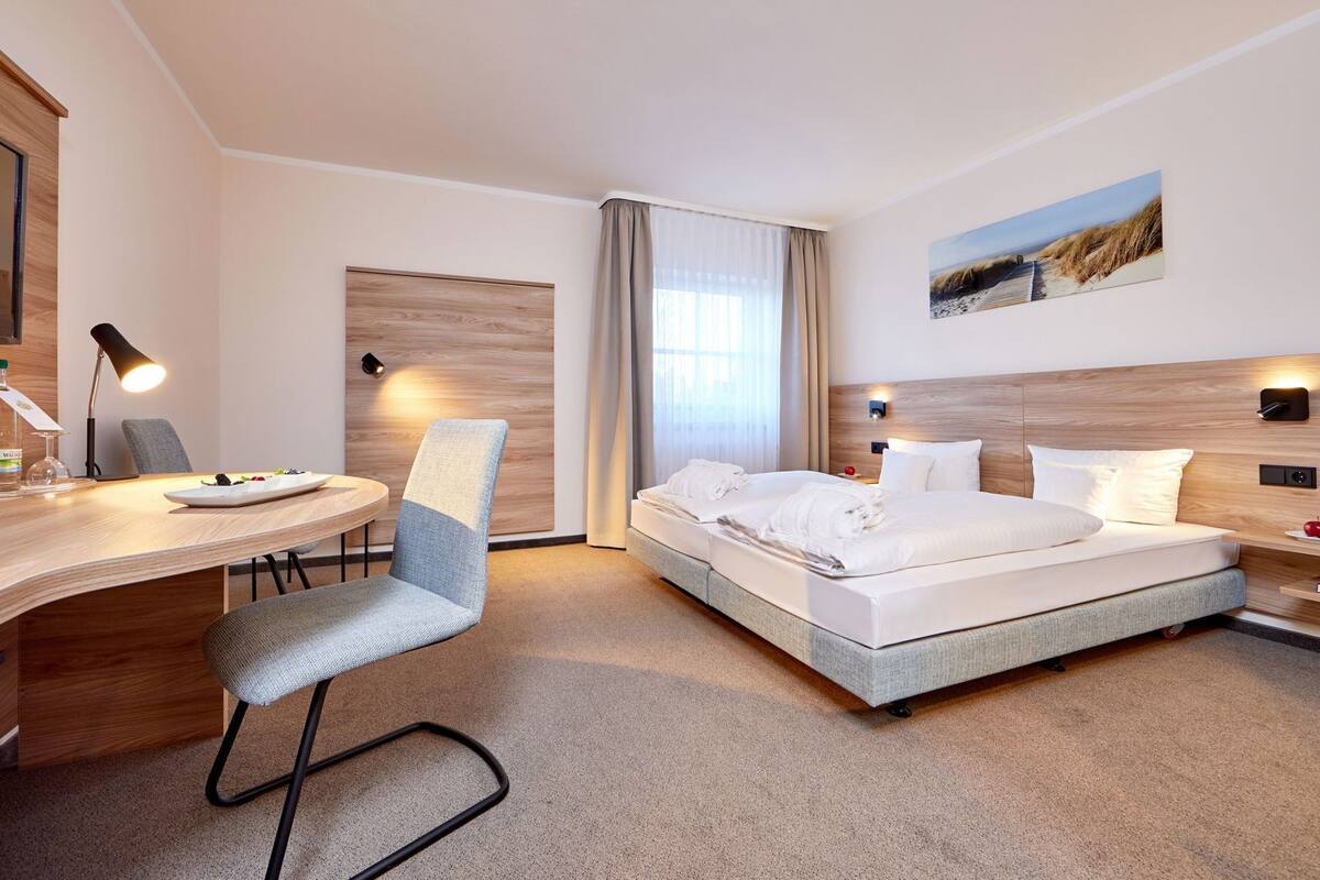 A hotel room with a bed, desk, chair, and a painting on the wall.