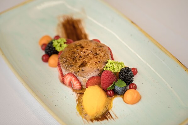 A dessert plate with a slice of cake, strawberries, raspberries, blackberries, and a dollop of yellow sauce.
