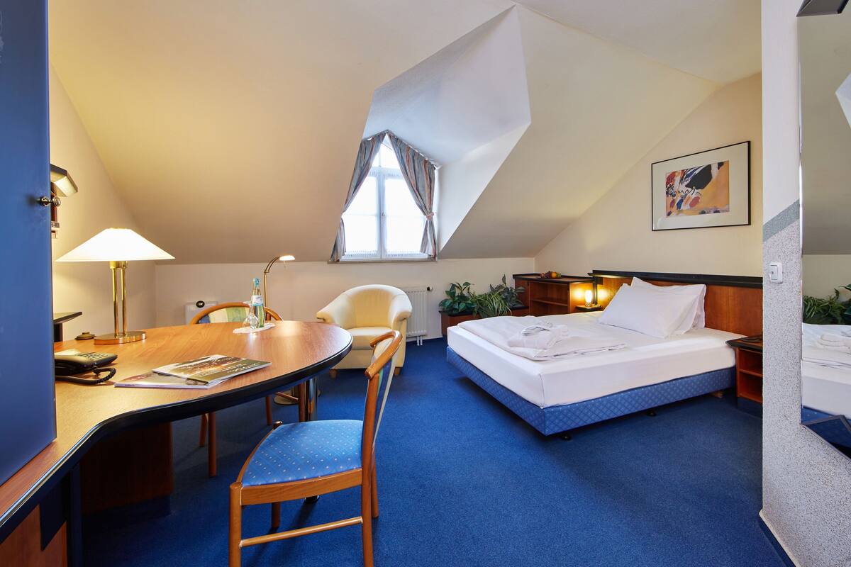 A hotel room with a bed, desk, chair, and a window with curtains.