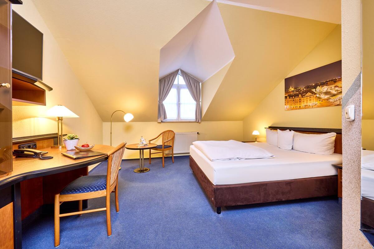 A hotel room with a bed, desk, chair, and a window with curtains.