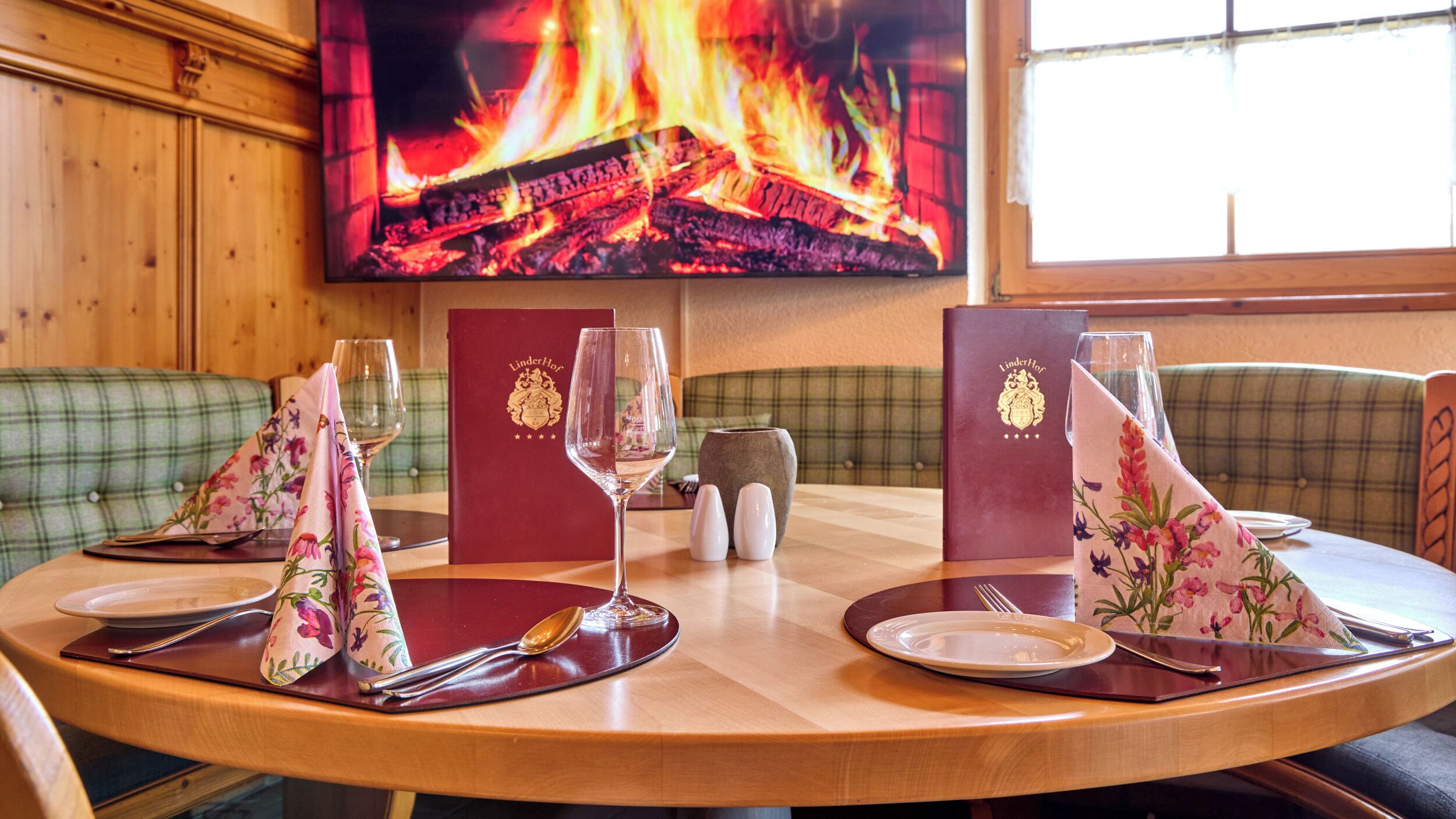Una mesa de comedor dispuesta con platos, cubiertos y servilletas, con una chimenea al fondo.