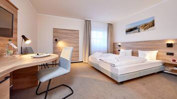 A hotel room with a wooden desk, a chair, a bed with white linens, a painting on the wall, and a window with curtains.