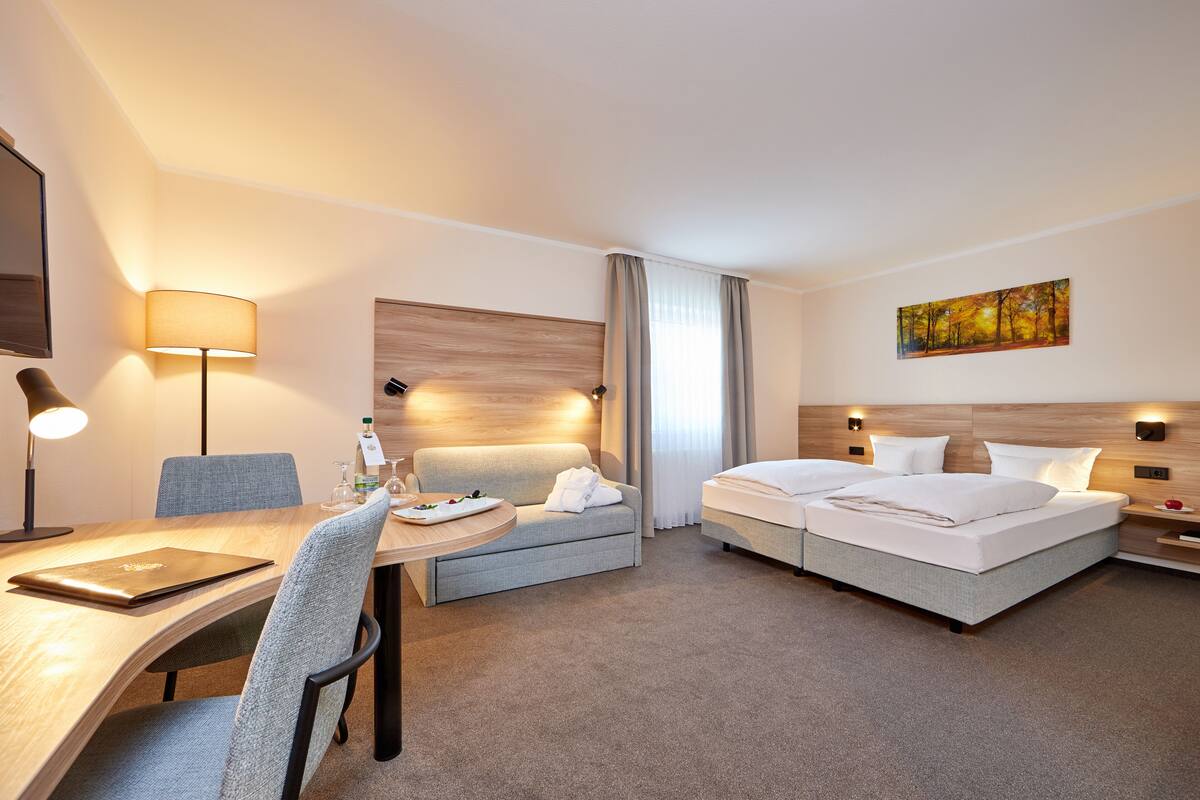 A hotel room with a bed, a sofa, a desk, and a lamp.