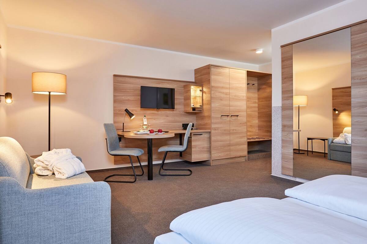 A hotel room with a bed, a desk with a chair, a TV, and a wardrobe.