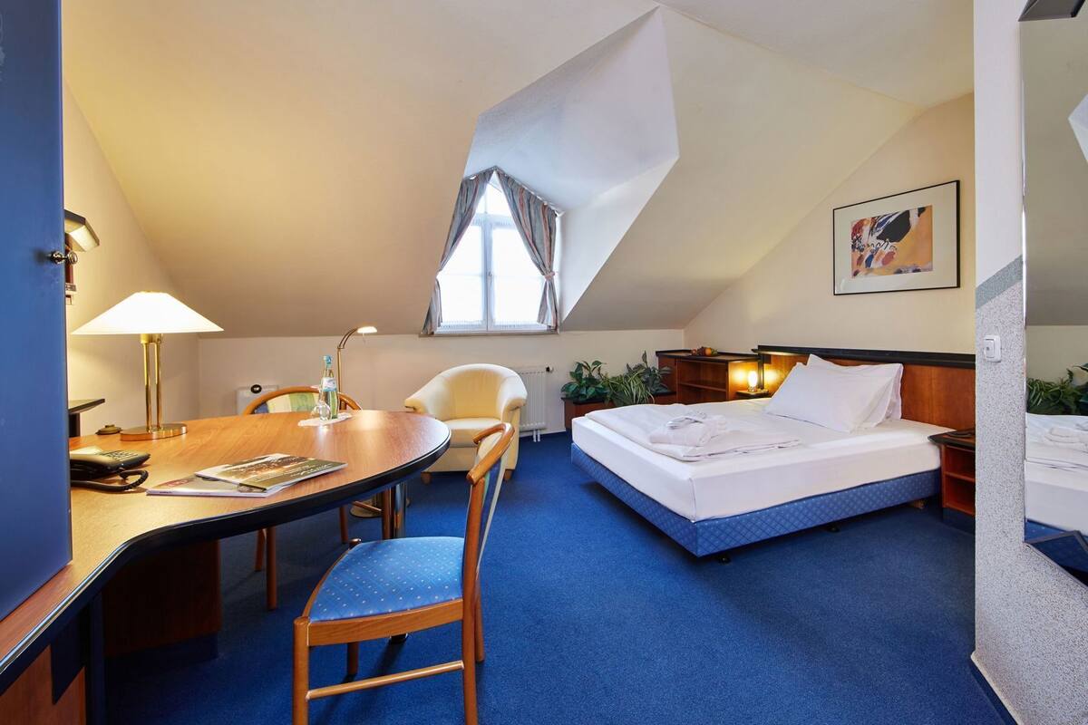 A hotel room with a desk, chair, bed, and a window with curtains.