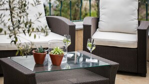 A wicker sofa with white cushions, a glass table with two potted plants, and a glass of water. - Hotel LinderHof Erfurt (Erfurt)