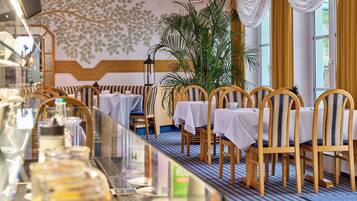 Un restaurant avec des chaises et des tables en bois, une grande plante en pot et un sol à motifs.