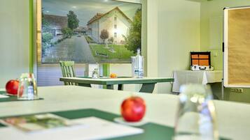A room with a large flat-screen TV displaying a scenic view, a table with a green tablecloth, two apples, a glass, and a bottle.