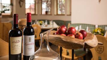 Two wine bottles and a pitcher on a table with a wooden bowl of apples in the background.