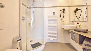 Un baño moderno con ducha de vidrio, lavamanos blanco y tocador con toallero.