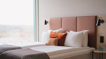 Habitación de hotel con cama, almohadas, mesita de noche y ventana con vistas.