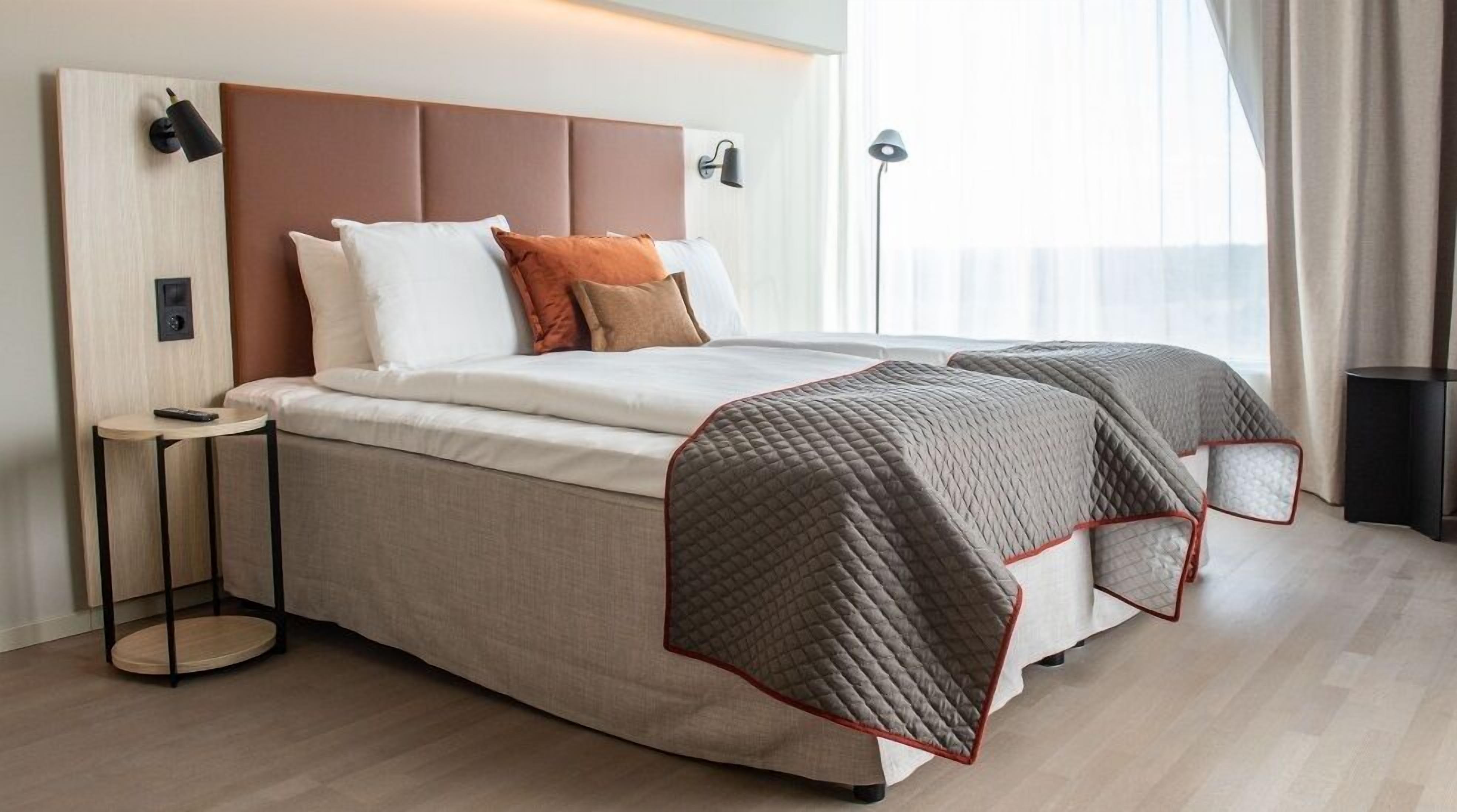 Een moderne hotelkamer met een groot bed, een nachtkastje, een lamp en uitzicht op de omgeving.