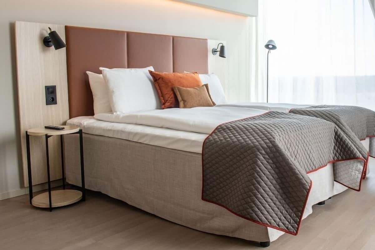 Une chambre d’hôtel moderne avec un grand lit, une table de chevet, une lampe et une vue sur l’extérieur.