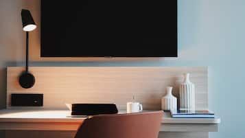 Quarto moderno com televisão de tela plana grande fixada na parede, uma escrivaninha com um laptop, uma cadeira e objetos decorativos.
