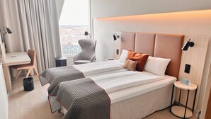 A hotel room with a large bed, a desk, a chair, and a view of the city through the window.