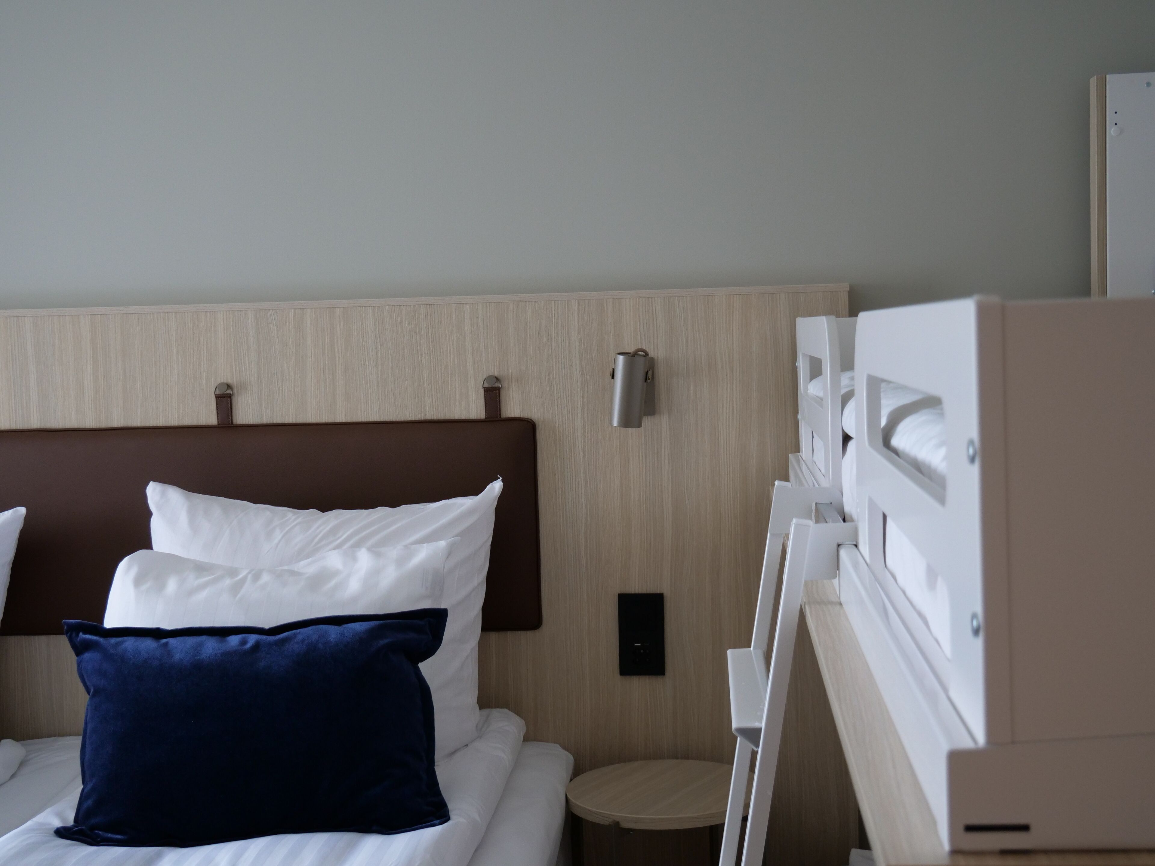 Et hotelværelse med en seng, puder, et natbord og en lampe på væggen.