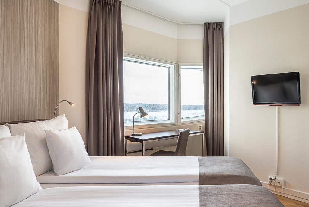 Een hotelkamer met een bed, bureau, stoel, televisie en een raam met gordijnen.