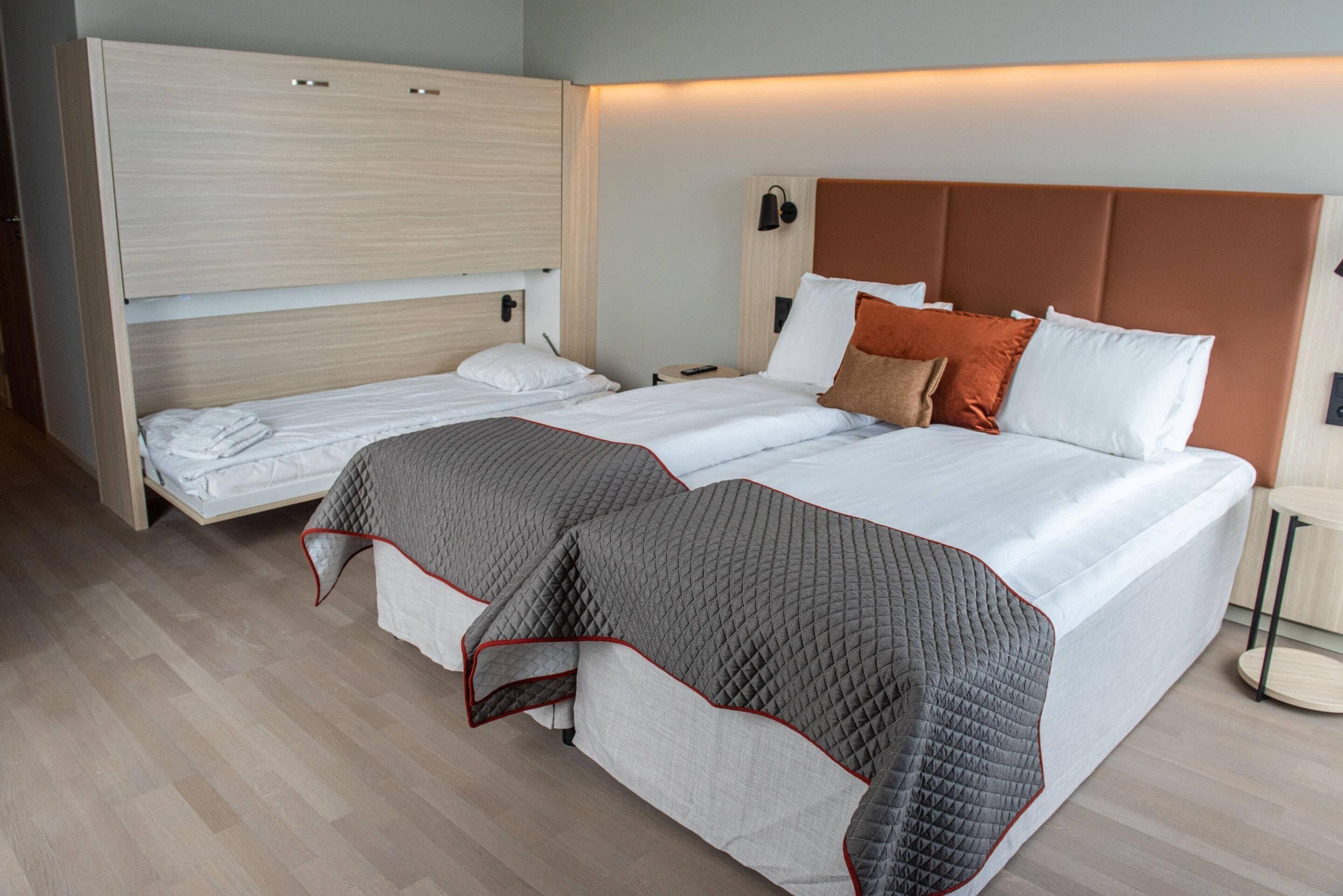 A double bed with a quilted blanket, a wooden wardrobe, and a bedside table with a lamp.