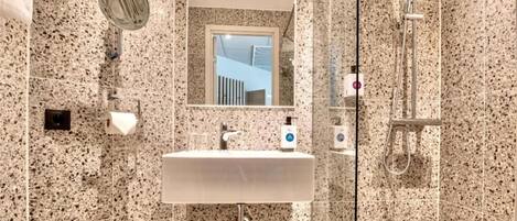 Un baño con lavamanos de encimera de granito, un espejo, una ducha y un dispensador de papel higiénico.