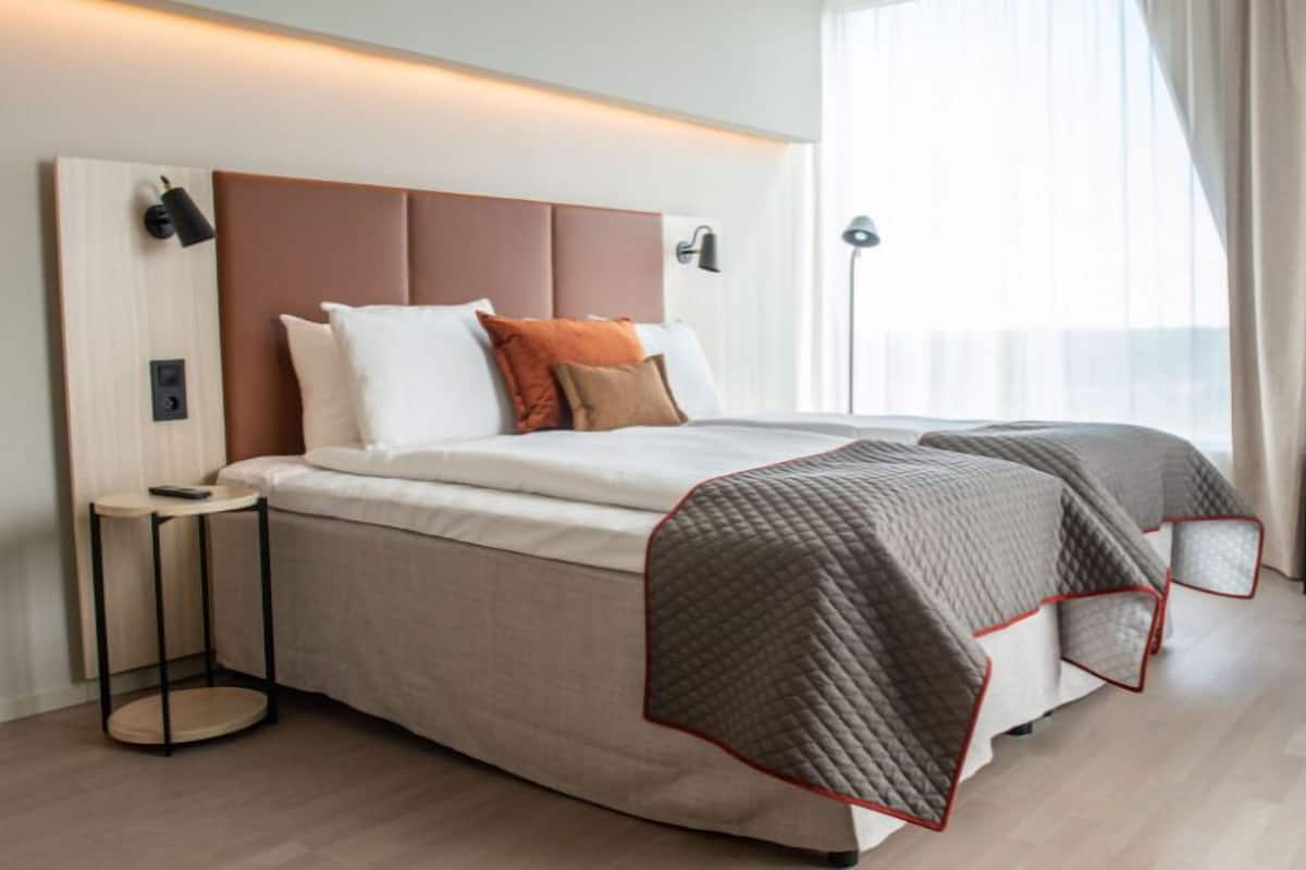 Een moderne hotelkamer met een groot bed, nachtkastjes, een lamp en uitzicht op het groen.