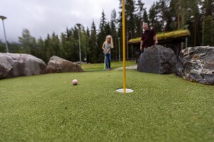 Césped artificial verde con una pelota de golf y una bandera amarilla.