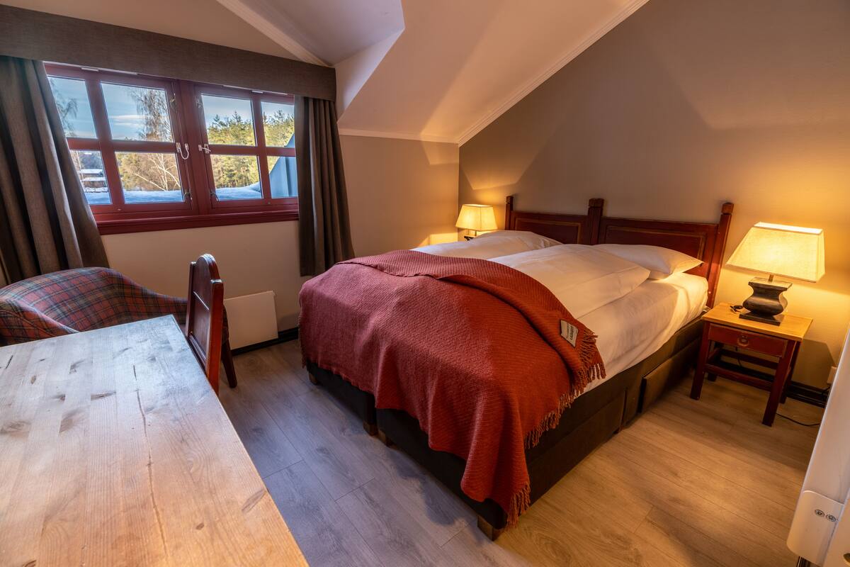 A bedroom with a bed, a nightstand, a chair, and a window with curtains.