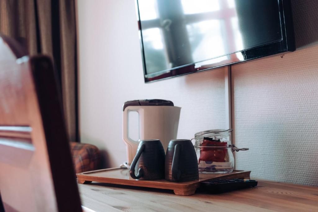 Una bandeja de madera con una cafetera, dos tazas, un frasco de azúcar y un control remoto sobre una mesa.