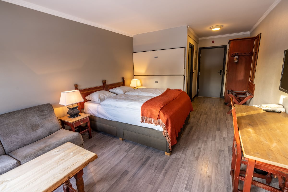 A hotel room with a bed, a sofa, a wooden table, and a lamp.