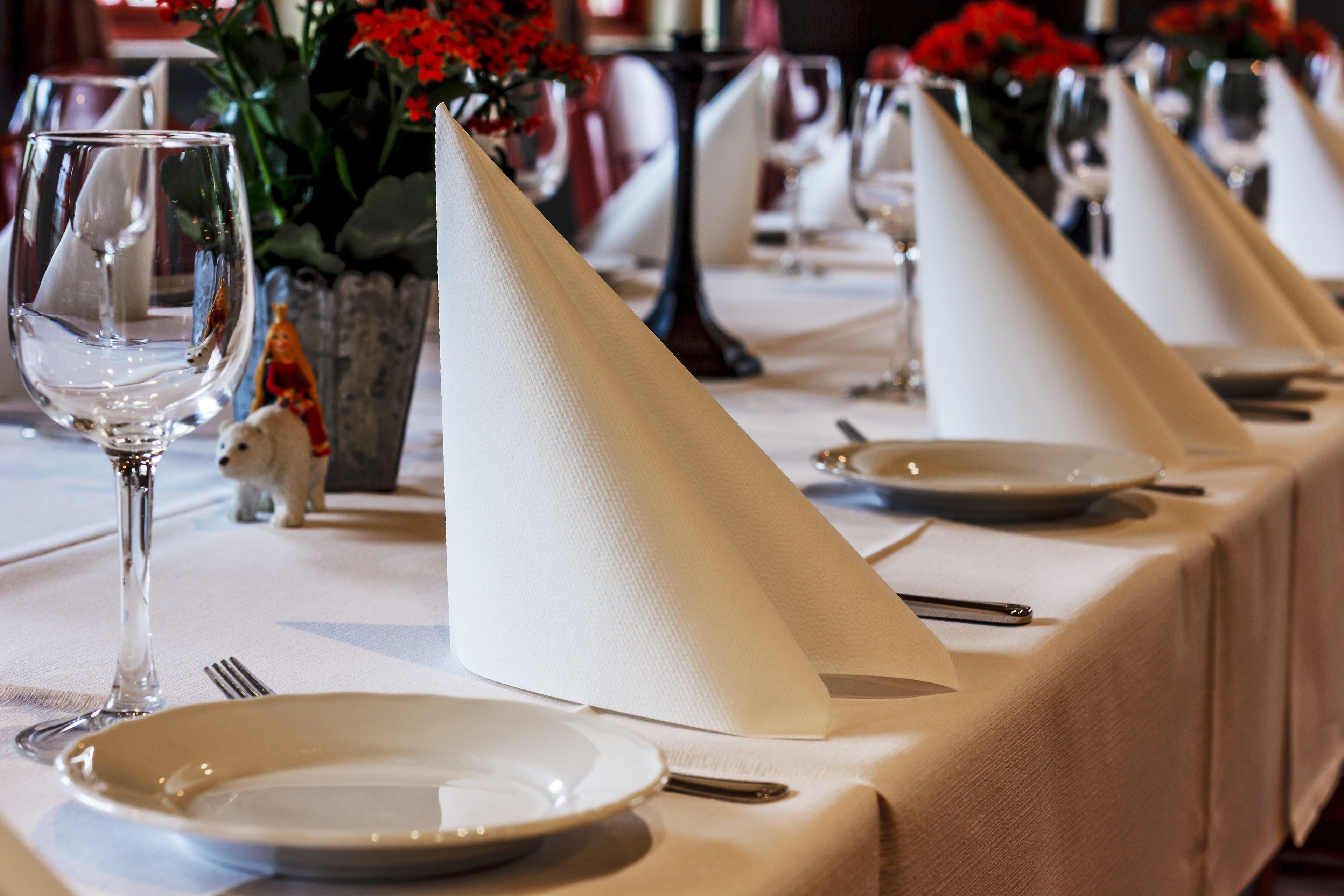 A dining table set with white tablecloths, plates, and silverware.
