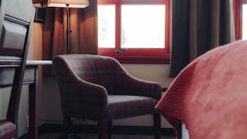 A plaid armchair by a window with a lamp and a bed in the foreground.