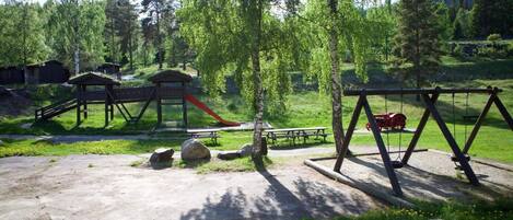 A playground with swings and a slide, surrounded by trees and a picnic area.