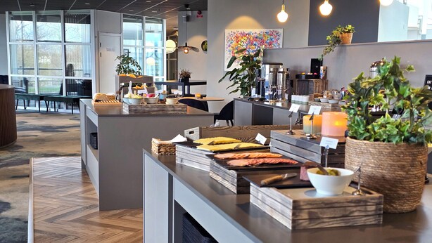 A modern breakfast bar with a variety of food options, a coffee station, and a seating area with a view of the outdoors.